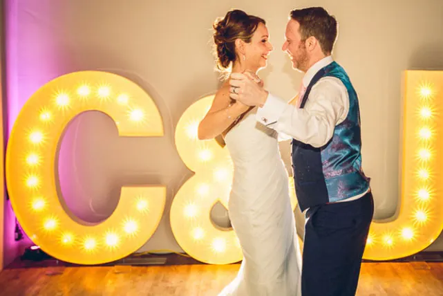 A couple dancing together in front of large illuminated yellow letters at an event venue.