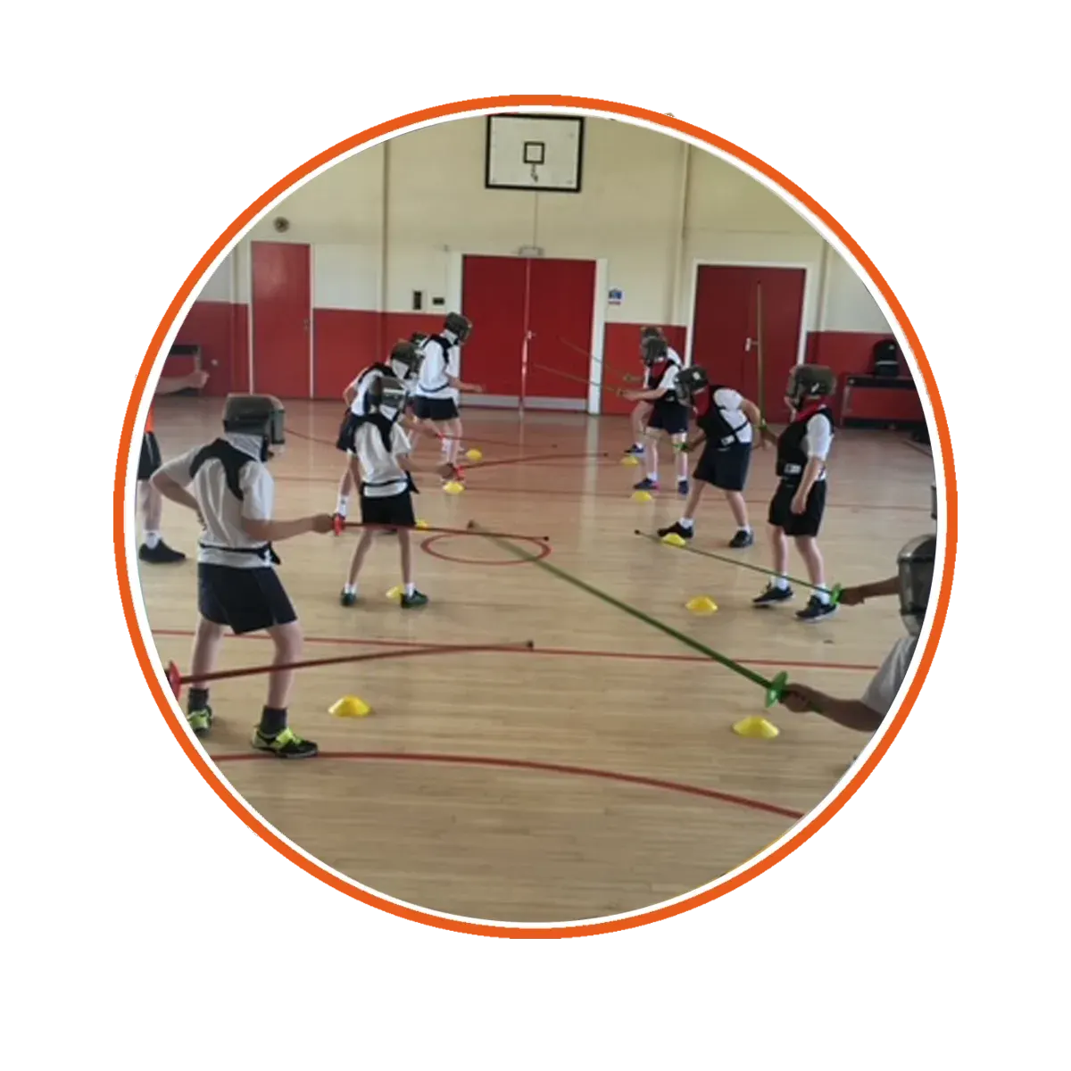 Young people in sports kit doing a training drill in a gymnasium with yellow marker cones on the wooden floor.
