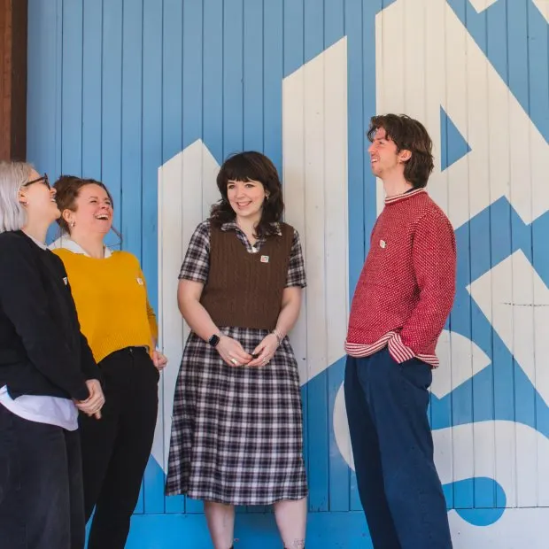 Four people stand chatting against a blue and white geometric mural.