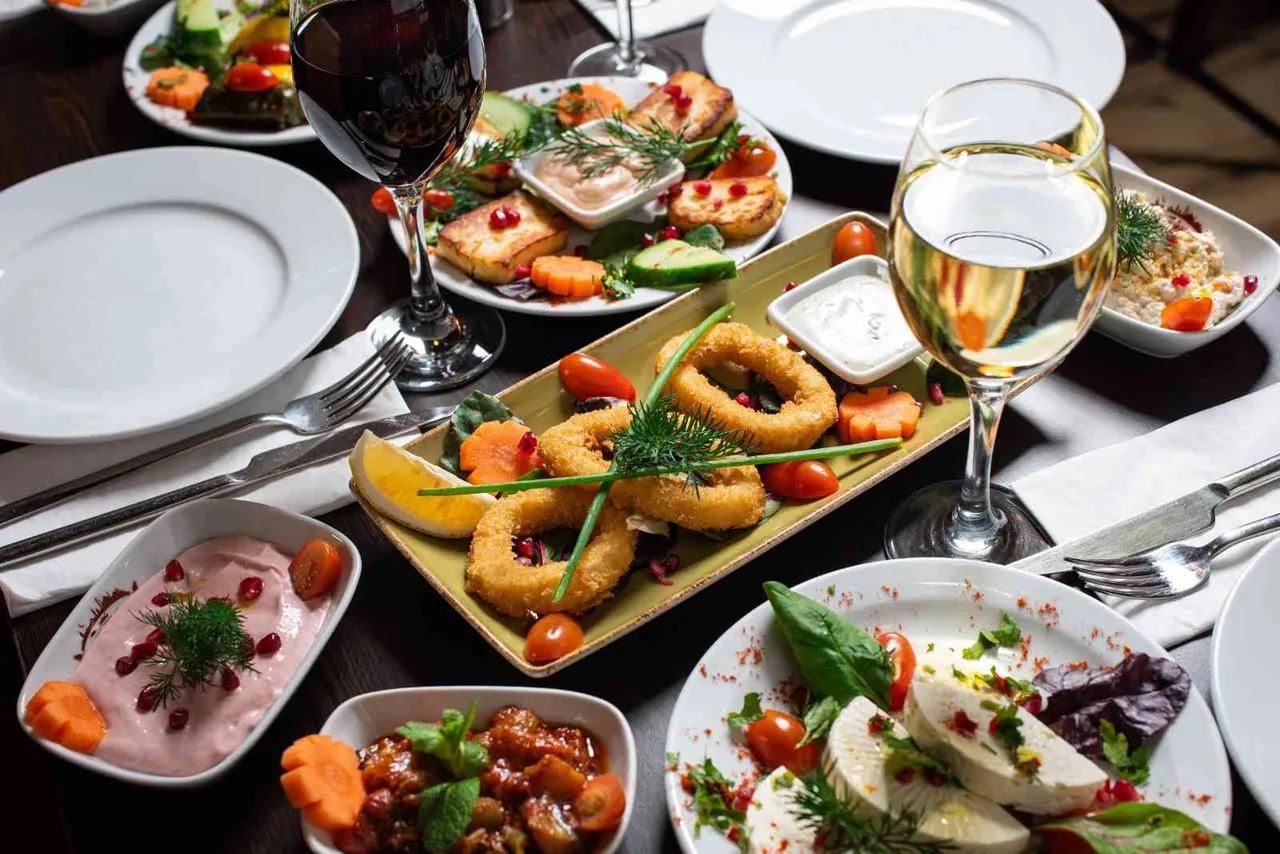 A table set with multiple dishes including fried calamari, seafood platters, and appetisers, accompanied by glasses of red wine and white wine.