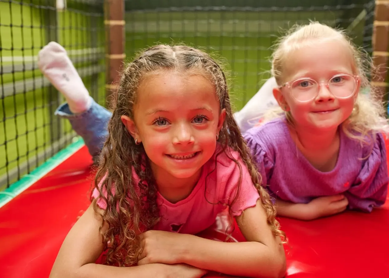 Two young children smiling on a red inflatable structure in an indoor play area.