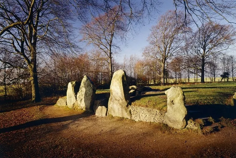 Stone burial chamber surrounded by bare trees and open parkland in winter sunlight.