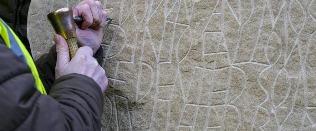 Person using a brush to clean carved stone surface in outdoor setting.