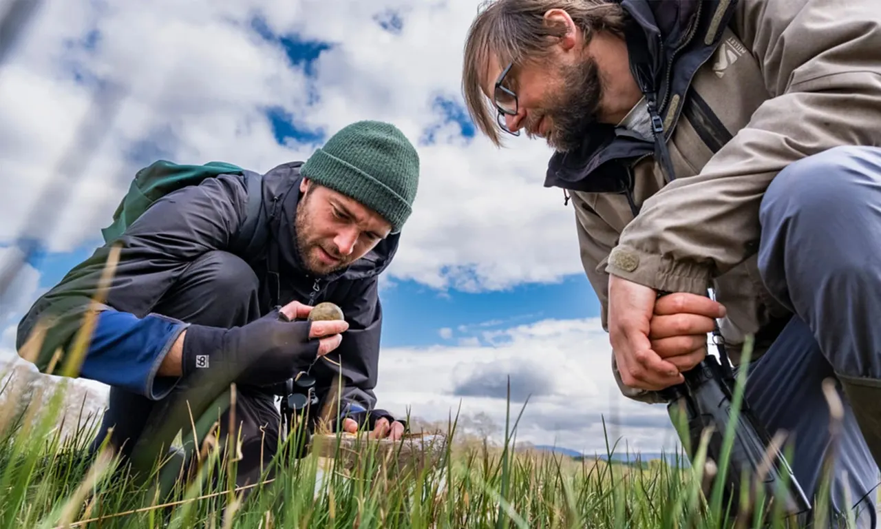 Two people examining wetland plants during an outdoor wildlife activity by a loch.