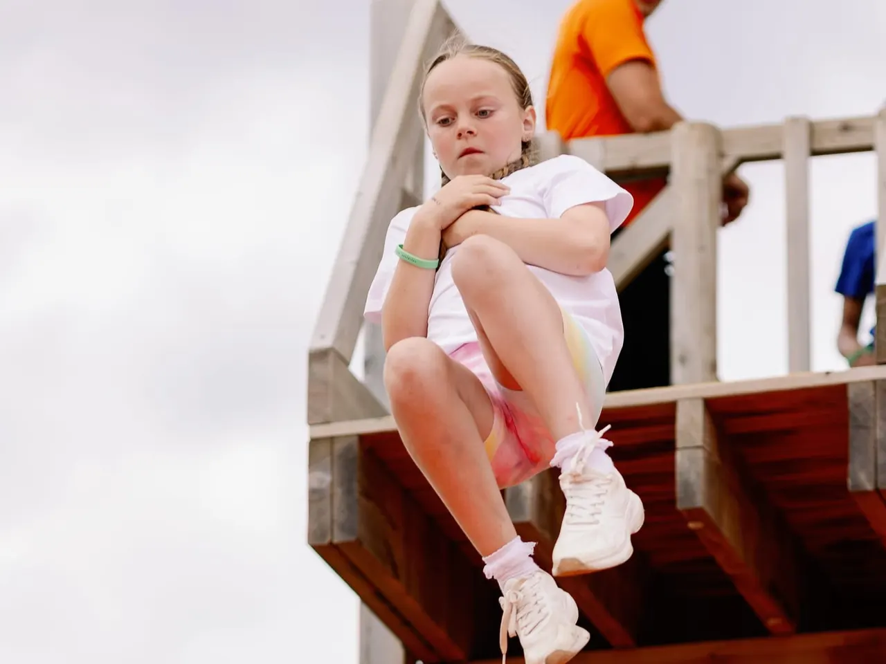 Child jumping off a wooden play structure at an outdoor leisure venue.