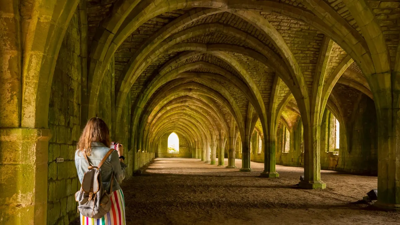 Woman taking a photograph inside a vaulted stone archway at a historic abbey ruin.