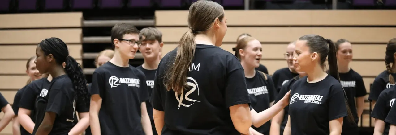 Group of young people wearing matching black team shirts gathered in a gymnasium or studio space.