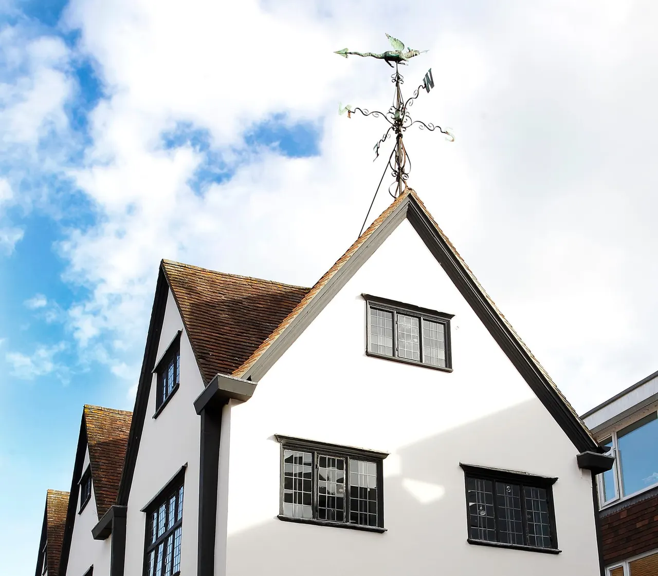 Traditional half-timbered building with white walls and dark timber framing, topped by a decorative weather vane against blue sky.