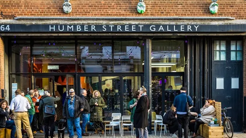 Visitors gathered outside and inside a brick gallery storefront with large windows on a busy street.