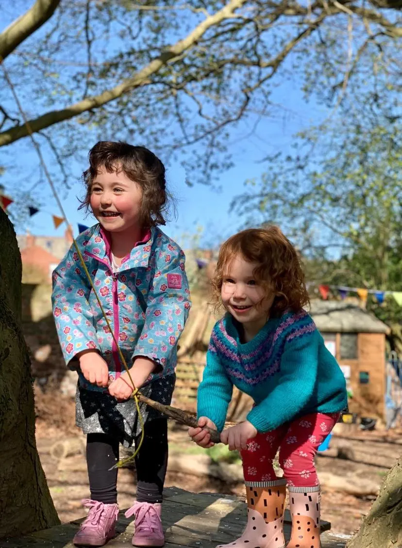 Two young children playing outdoors beneath bare tree branches on a sunny day at a rural venue.