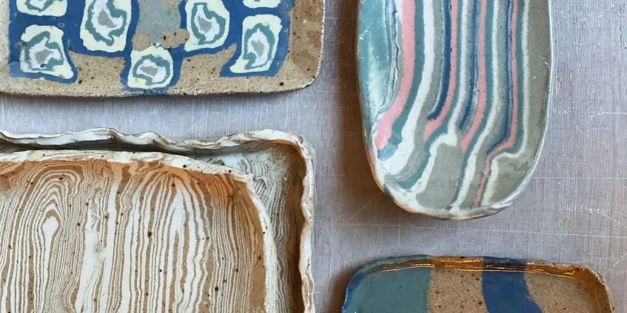 Close-up of four handmade ceramic dishes with varied glazed patterns in blue, cream, brown and marbled designs.