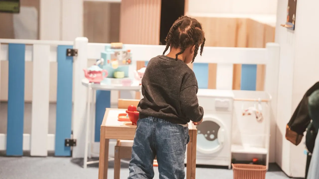 Child playing at a pretend kitchen and laundry station in an indoor play area.