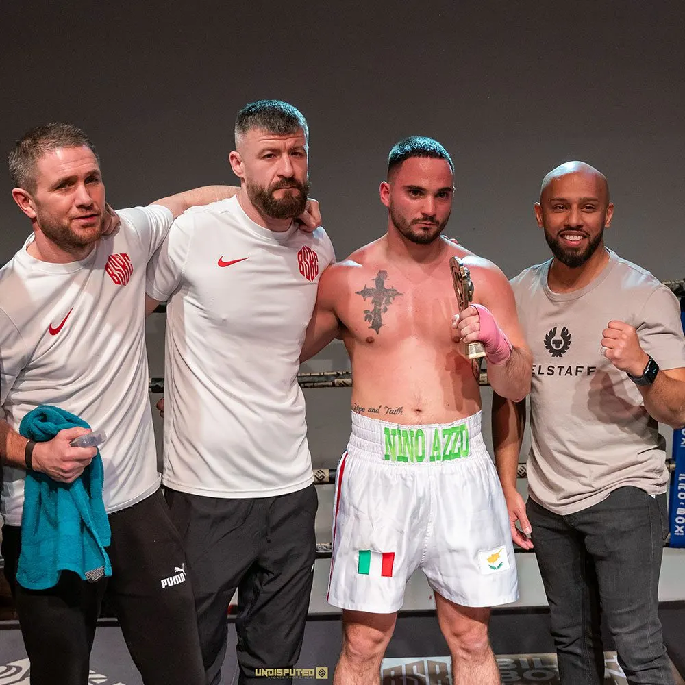 Four men pose together after a boxing match, with the shirtless boxer in the centre holding a trophy.