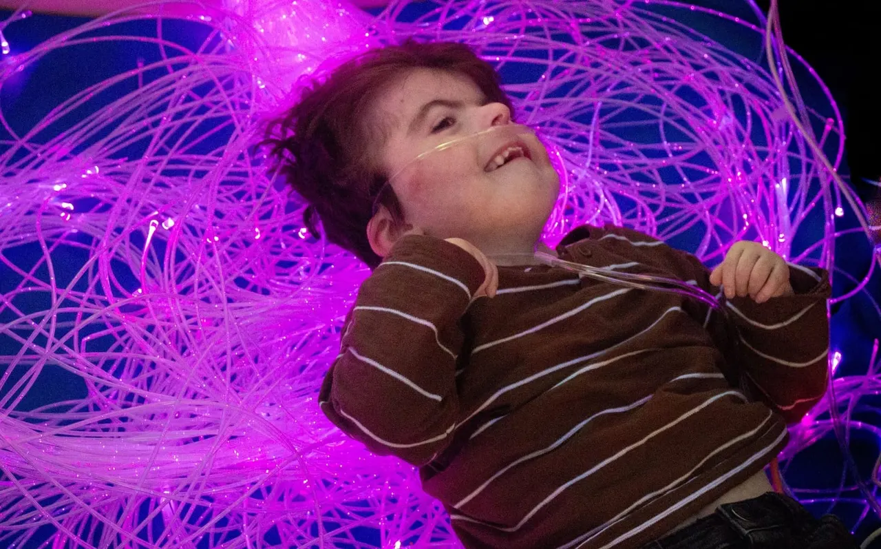 Child smiling and looking up surrounded by bright purple glowing neon fibre optic lights.