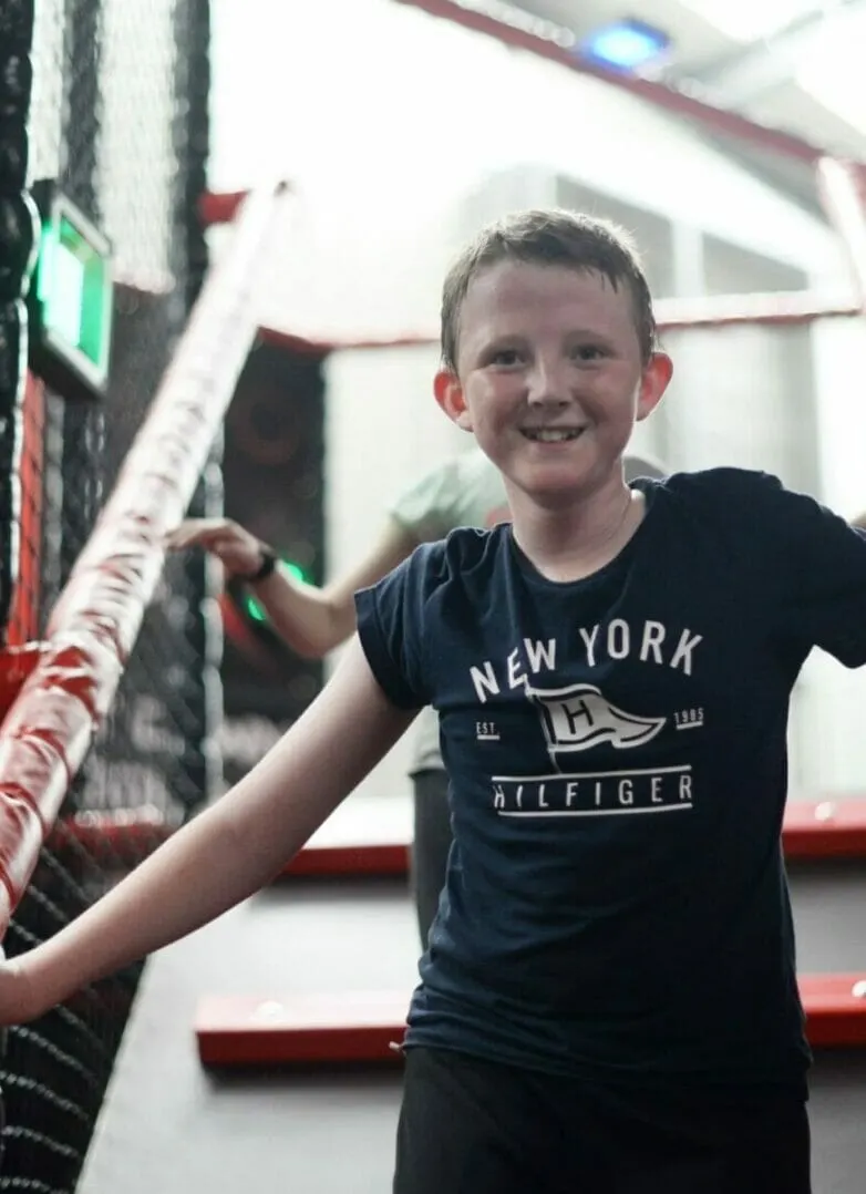 Young child smiling whilst playing on indoor soft play equipment with padded climbing structures.
