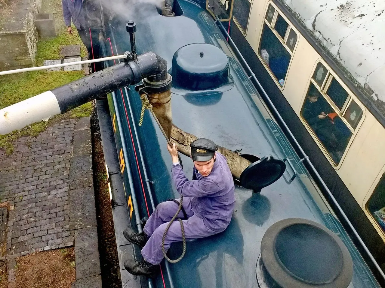 Canal boat captain in purple uniform handling mooring rope on narrow boat deck.