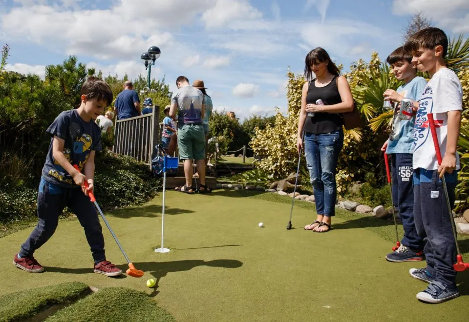 Children playing crazy golf on a bright day, with tropical plants and landscaping surrounding the course.