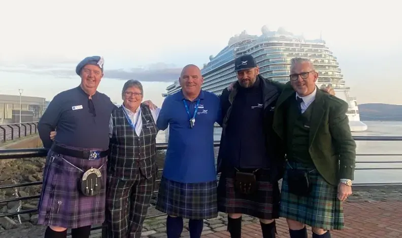 Five men in kilts and formal wear stand together on a dock with a large cruise ship in the background.