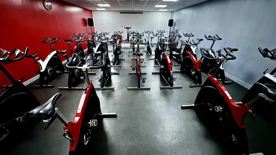Rows of stationary exercise bikes in red and black lined up in a bright studio with red and white walls.
