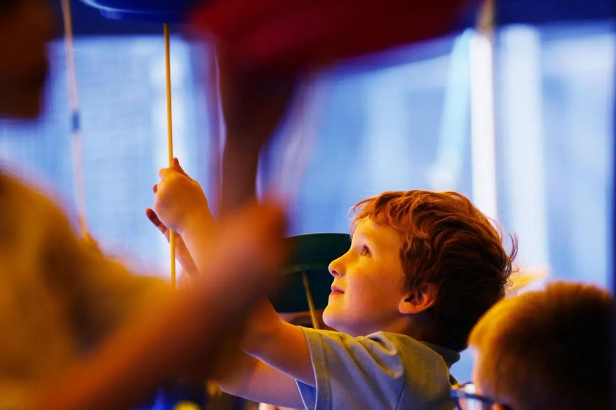 Child reaching up to touch a suspended circus prop during an interactive performance.