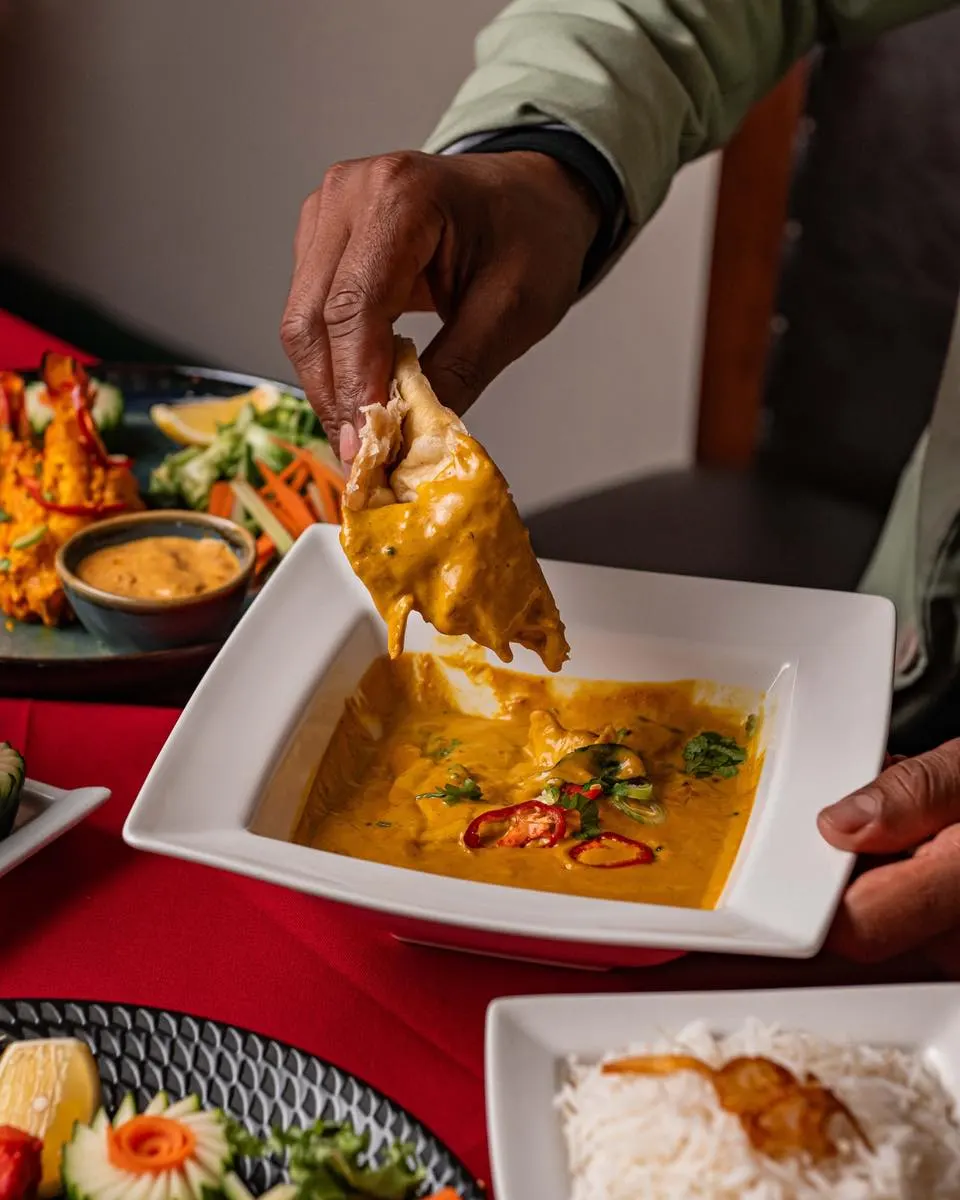 Person dipping crispy fried wonton into golden curry sauce at a dining table.