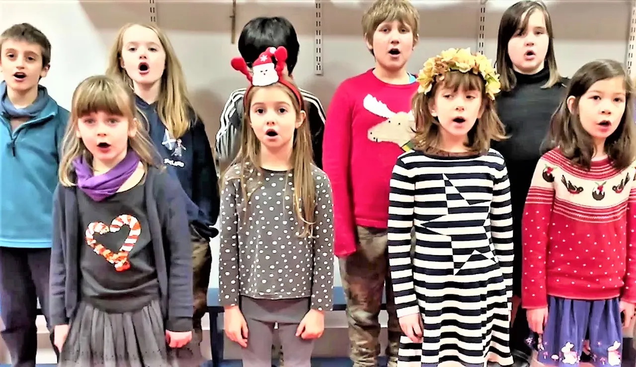 Group of children singing together in a choir performance, wearing colourful casual clothing.