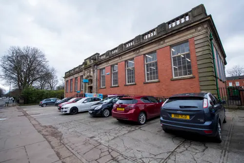 Historic red brick building with parked cars in front and bare trees under cloudy sky.