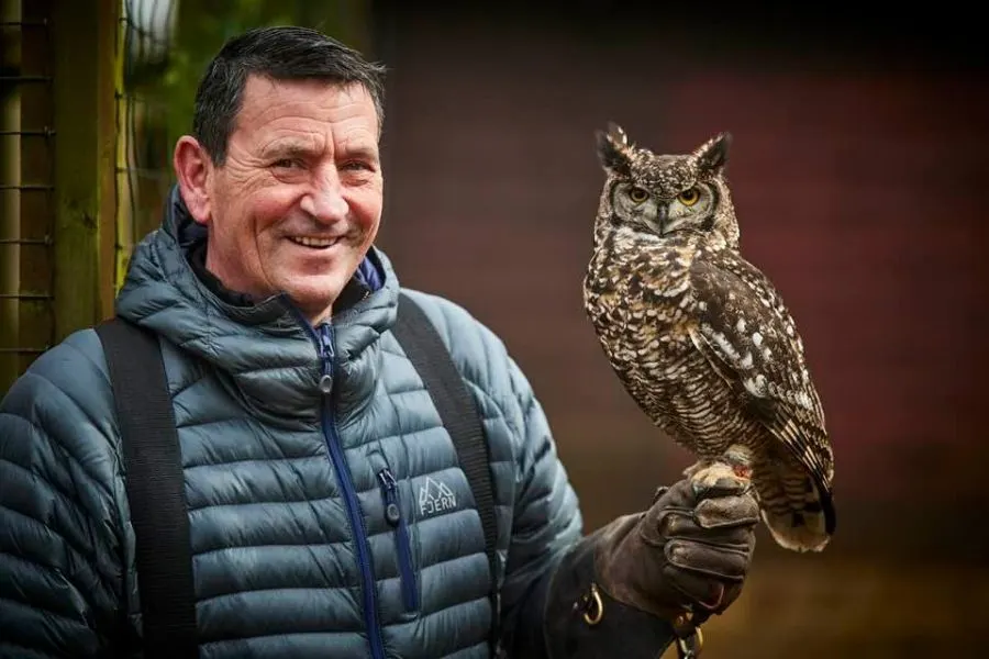 Man in black padded jacket holding an eagle owl on his gloved hand.