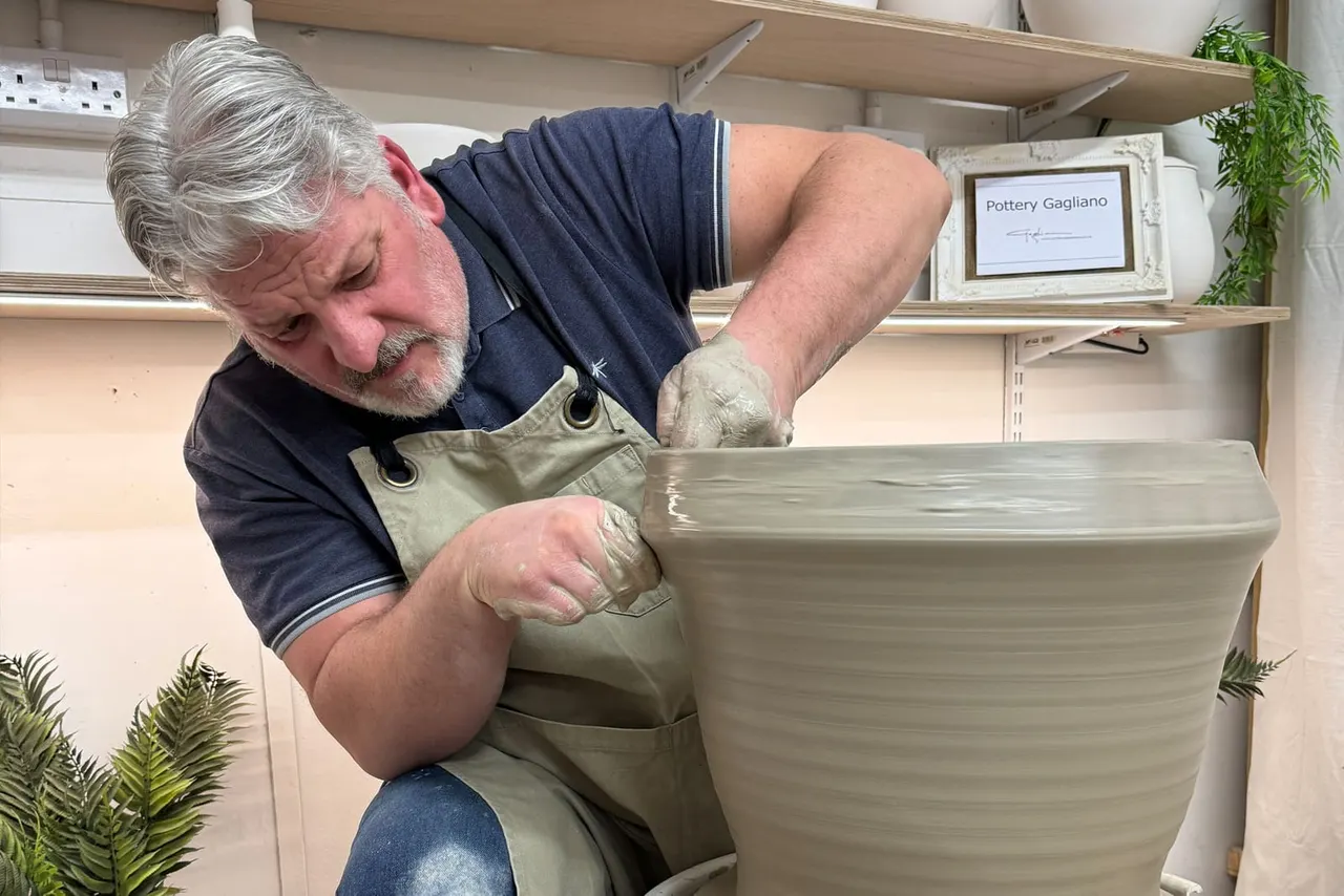 A potter working on a large ceramic vessel at a pottery wheel in a studio workshop.