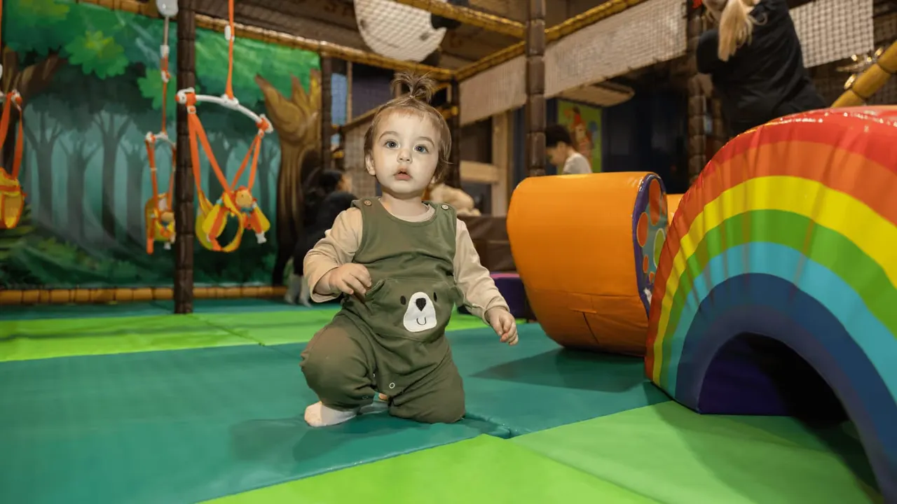 Toddler crawling through indoor play area with coloured tunnels and hanging rope toys.