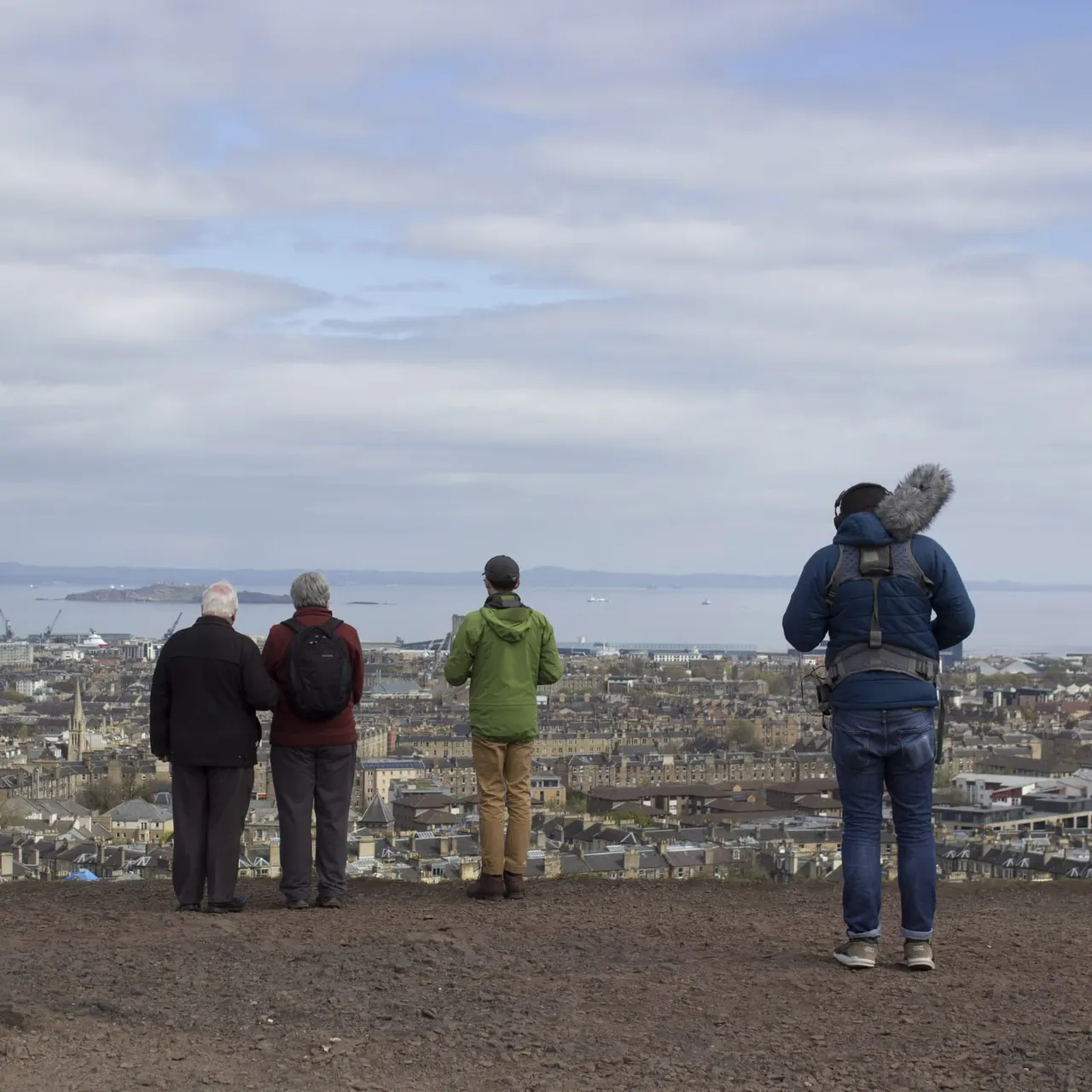 Four visitors standing on an elevated viewpoint overlooking a coastal city and bay.