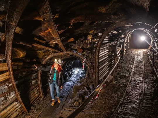 Visitor in hard hat standing on underground mine railway tracks inside historic coal mine tunnel.