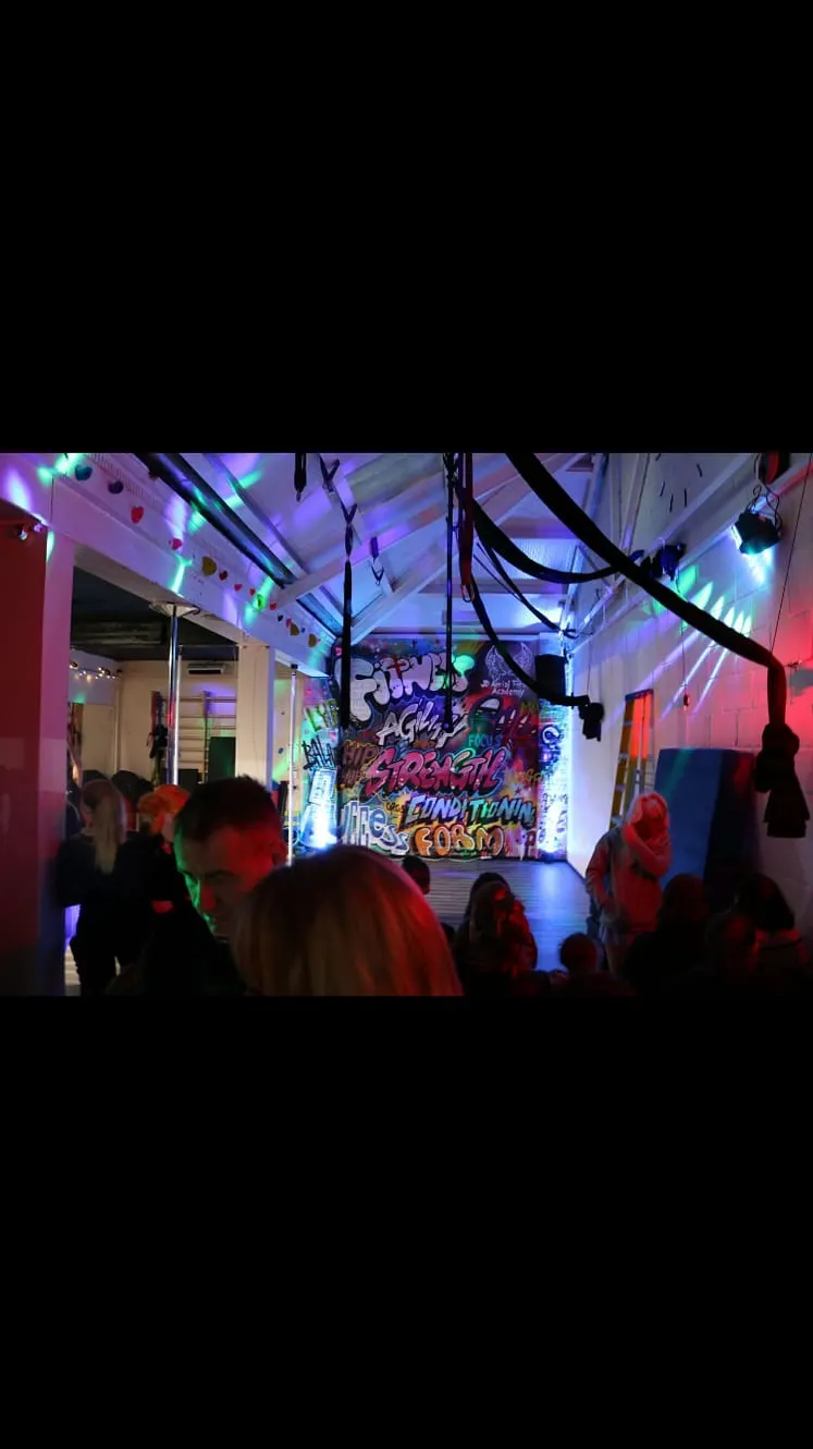 Children and adults enjoying a brightly lit indoor play space with colourful neon signs and hanging decorations.