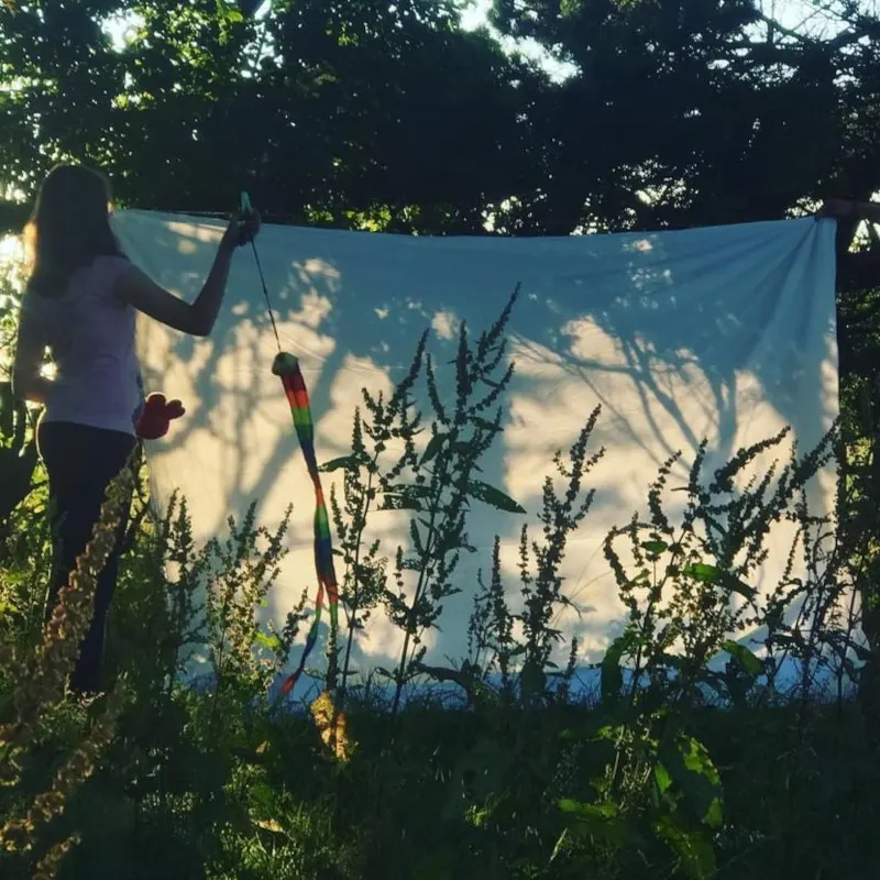 Woman hanging blue sheet to dry on outdoor washing line surrounded by wild plants and trees.