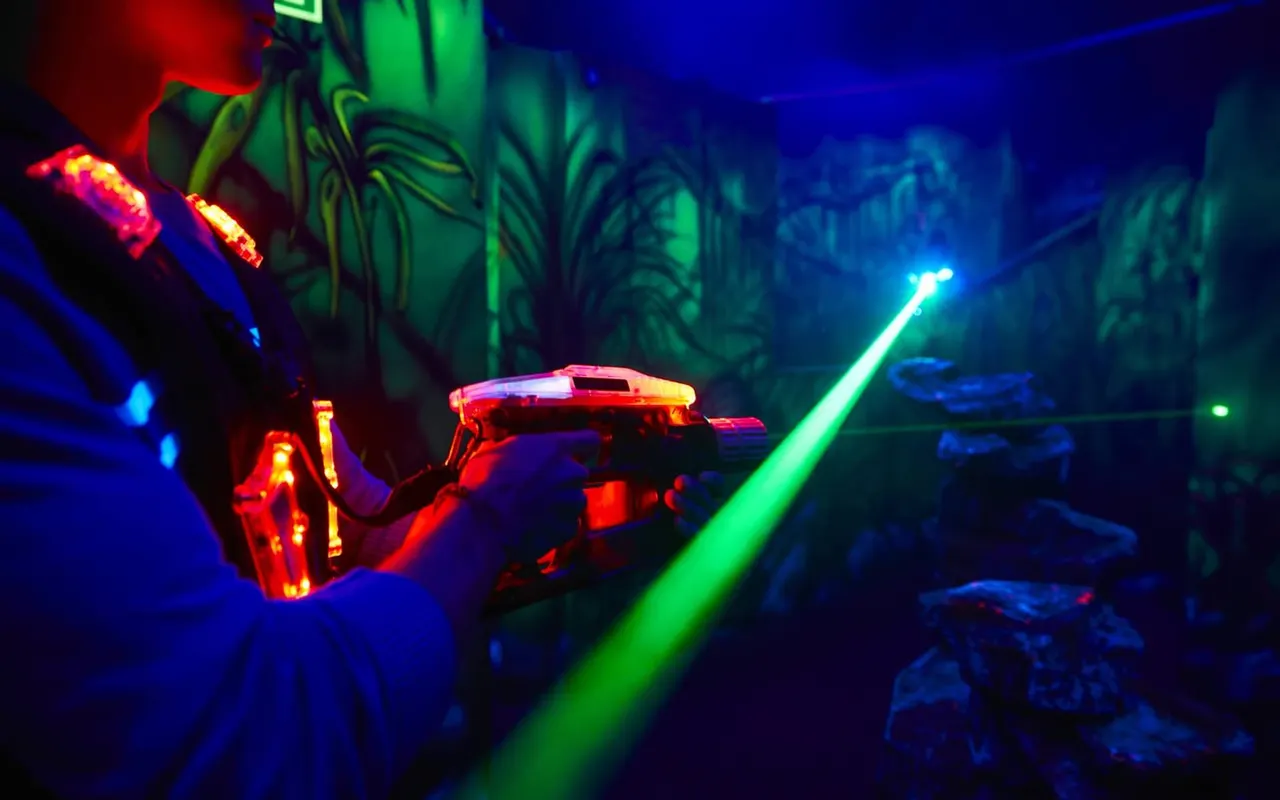 Players holding illuminated laser guns in a darkened arena with neon lighting and tropical-themed scenery.