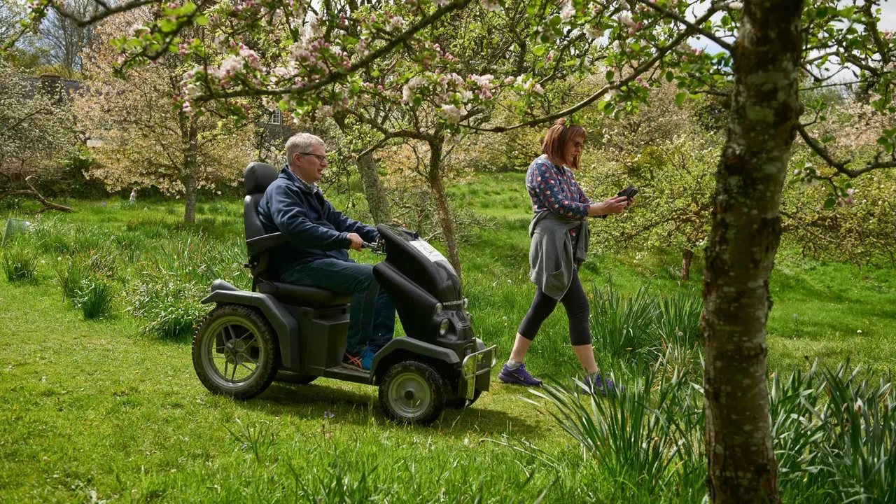 Man on mobility scooter and woman jogging through orchard with flowering trees in spring.