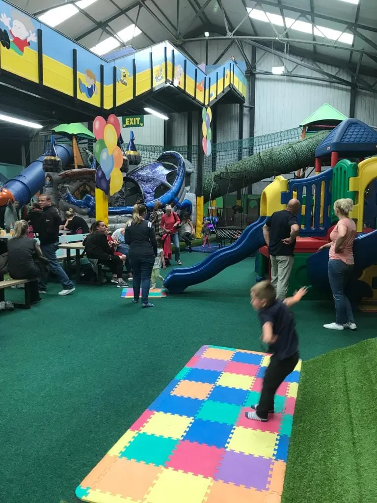 Children and adults playing in an indoor soft play area with slides, tunnels and climbing equipment.