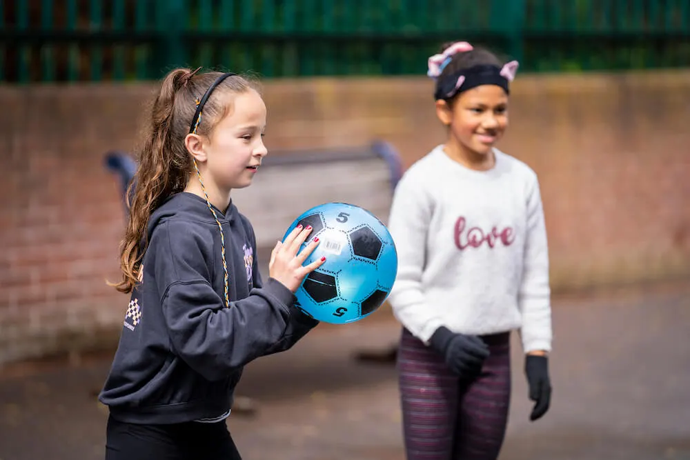 Two young children playing with a blue football in a sports court at a leisure venue.