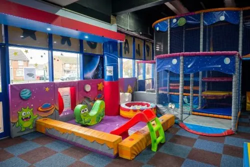 Colourful soft play area with slides, climbing frames and space-themed decorations for young children.