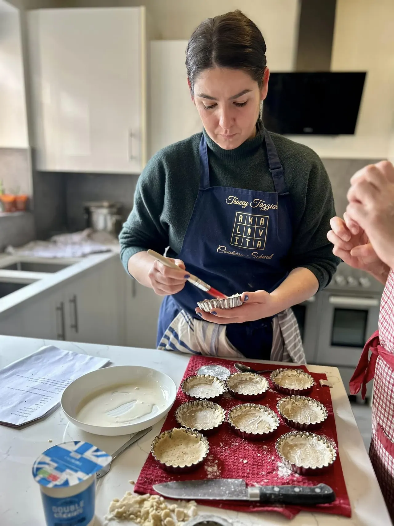 Instructor decorating individual tartlets with cream during a cookery class in a kitchen.