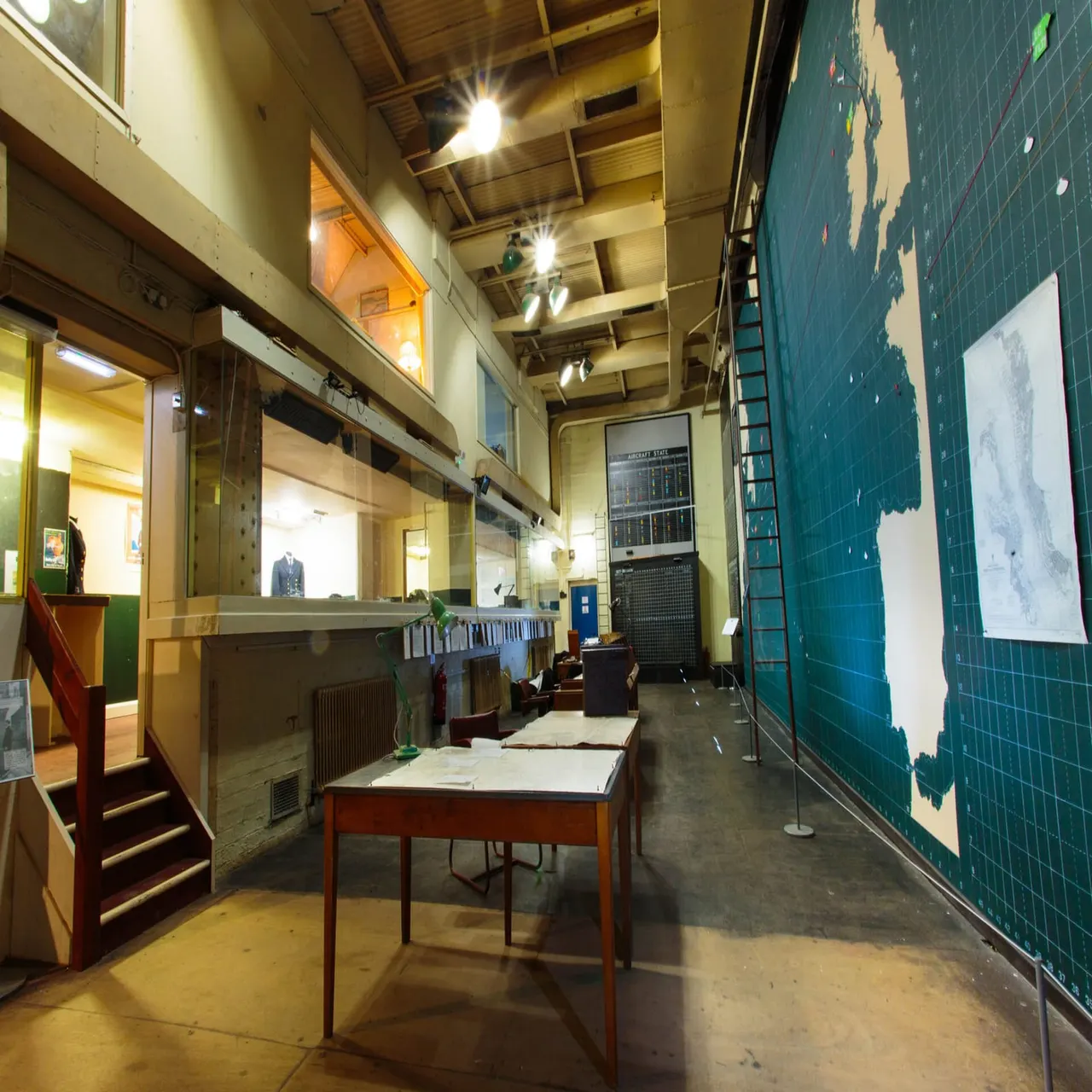 Interior corridor of a former military or government building with vintage furniture, maps on teal walls, and institutional fixtures.