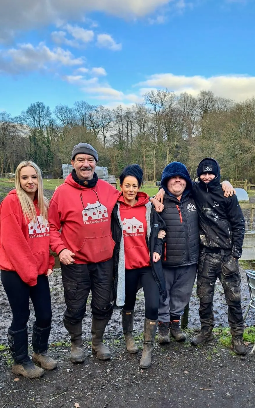 Five staff members posing together outdoors at a rural venue wearing branded red hoodies and winter clothing.