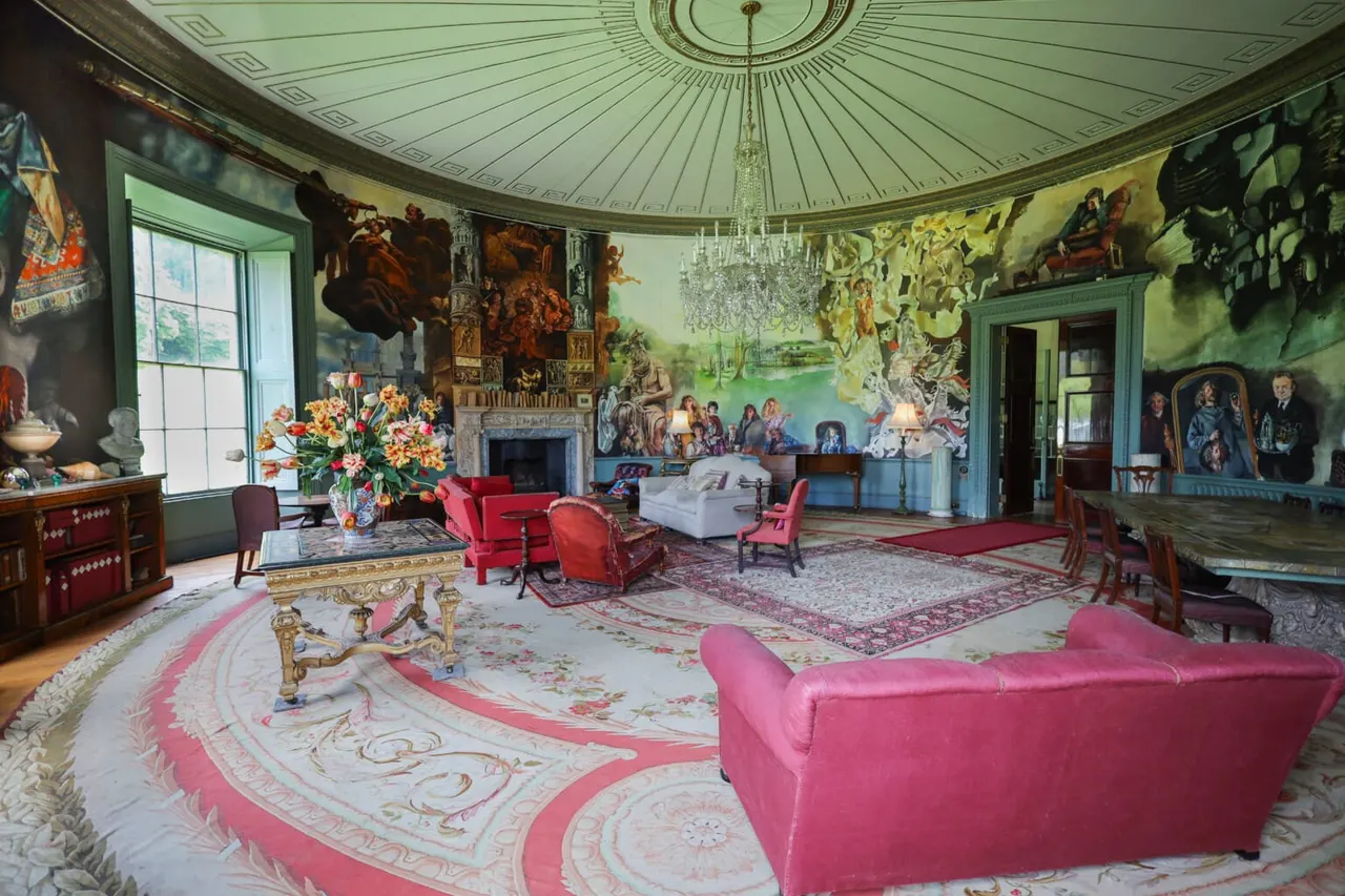 Ornate circular reception room with domed ceiling, pink velvet furniture, elaborate murals, crystal chandelier and period antiques.