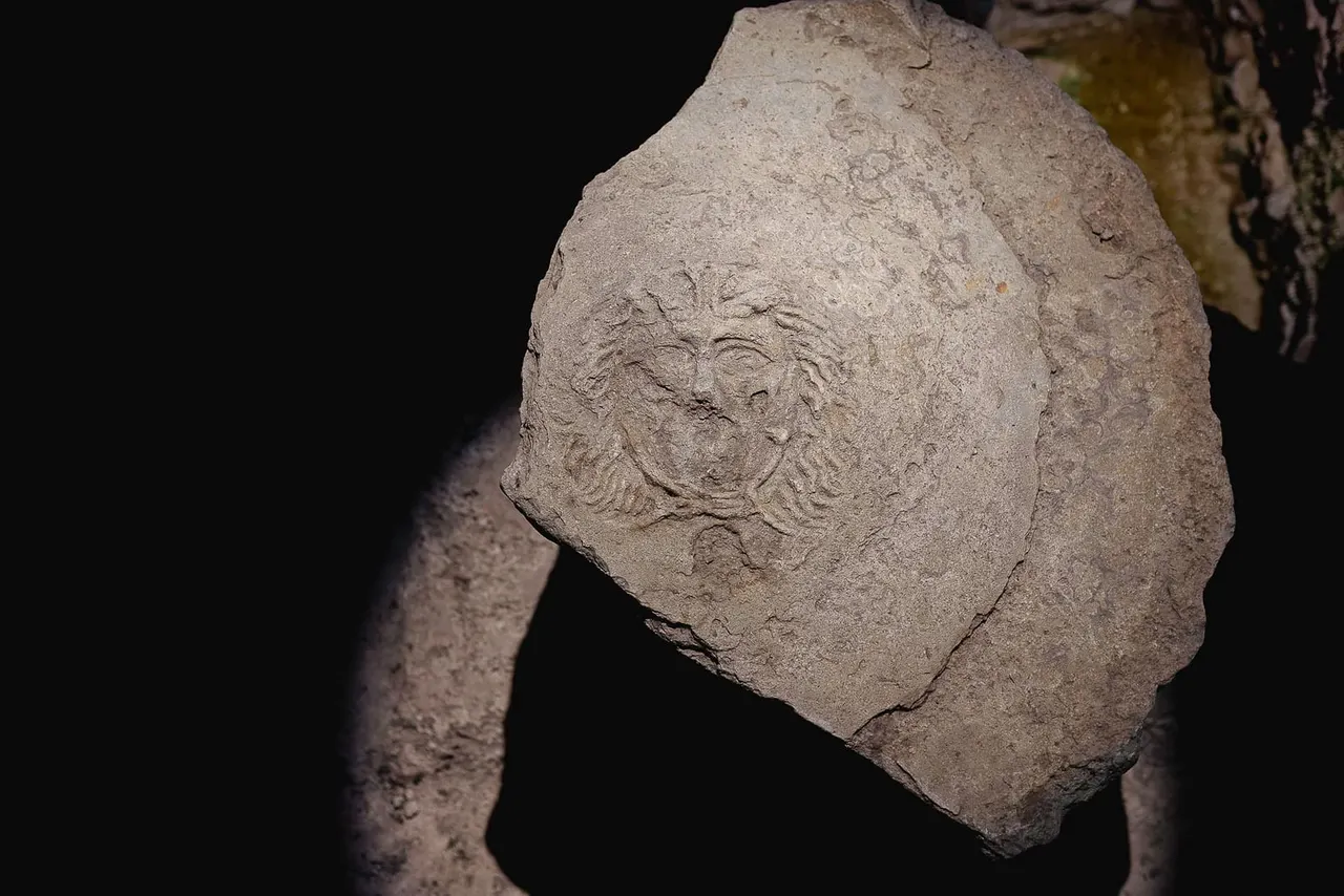 Stone relief carving of a bearded male face, displayed in museum lighting against a dark background.