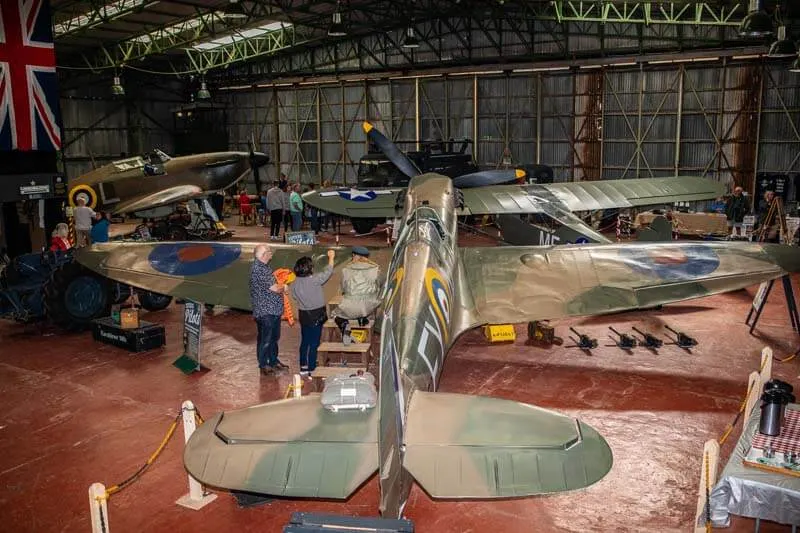 Visitors examine vintage military aircraft on display inside a large hangar.