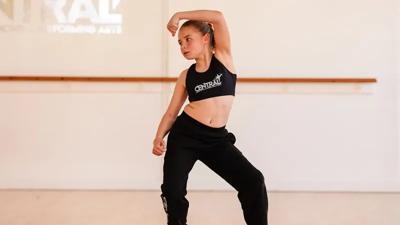 Young dancer stretching in a studio with a wooden barre on the wall.