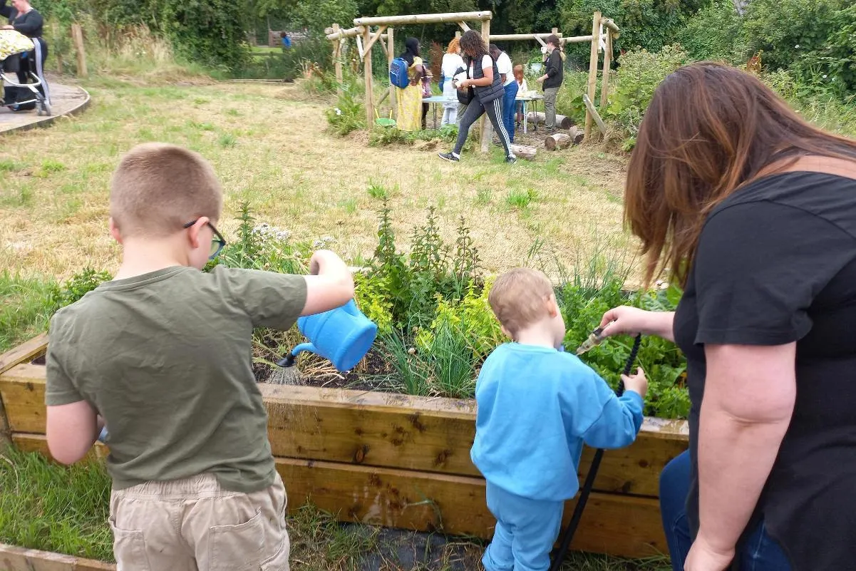 Young children and adults tending raised garden beds at an outdoor farm activity area.