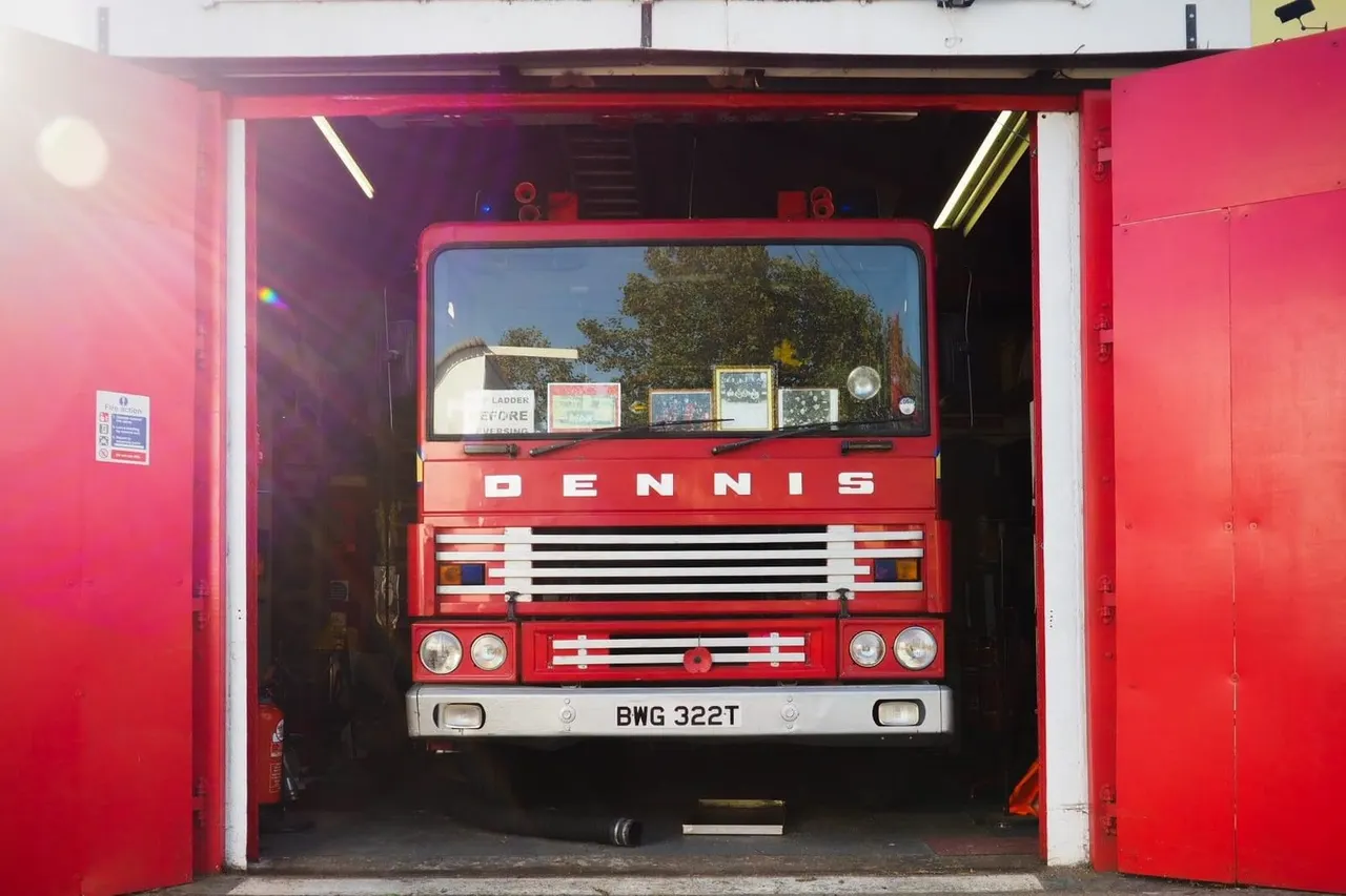 Red vintage Dennis fire engine displayed in a museum garage with registration plate visible.