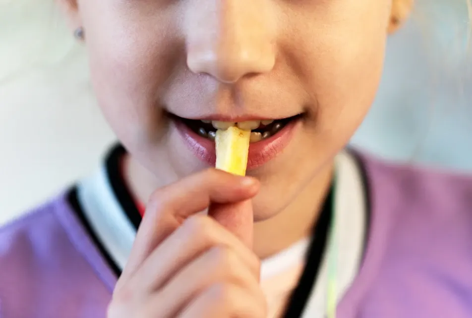 Child eating a yellow ice lolly outdoors.