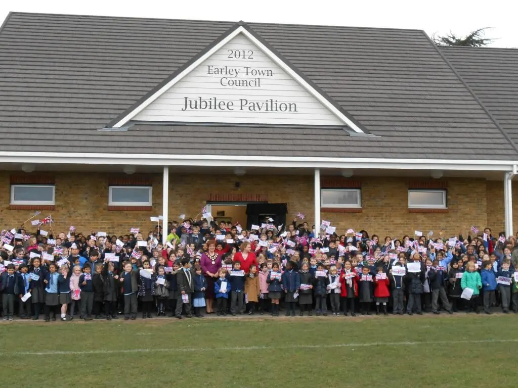 A large group of people of mixed ages gathered outside the Jubilee Pavilion, holding Union Jack flags and celebrating.